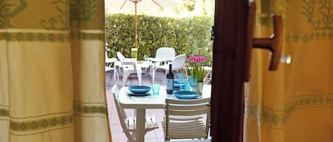 An outdoor dining area with a table set for two, white chairs, and a white umbrella.
