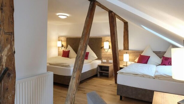 A room with two beds, wooden beams, and a sloped ceiling. - Alpengasthof zur Post GmbH (Schattwald)