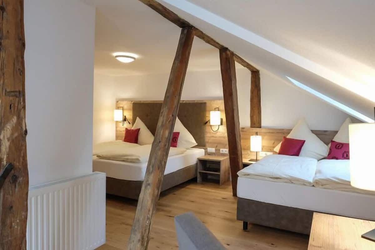 A room with two beds, wooden beams, and a sloped ceiling.