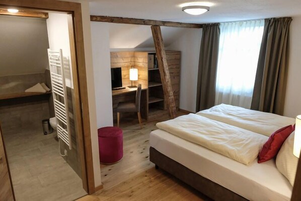 A bedroom with a bed, a desk, a chair, a TV, and a red ottoman. - Alpengasthof zur Post GmbH (Schattwald)