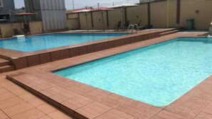 A rectangular swimming pool with tiled edges, surrounded by a low brick wall. - Droptop Suites (Lekki)