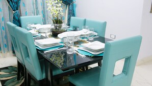 A dining table set with blue chairs, a vase with flowers, and a glass of water. - Droptop Suites (Lekki)