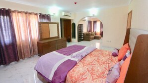 A bedroom with a bed, a dresser, a mirror, and a wardrobe. - Droptop Suites (Lekki)