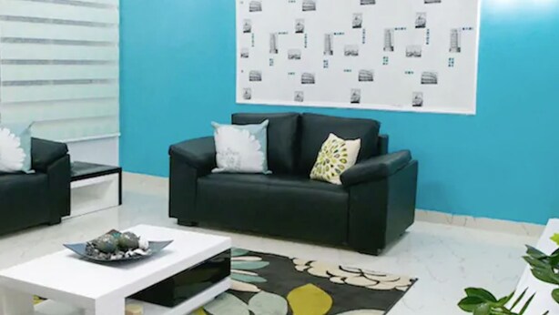 A modern living room with a blue accent wall, a black sofa, a white coffee table, and a patterned rug. - Droptop Suites (Lekki)