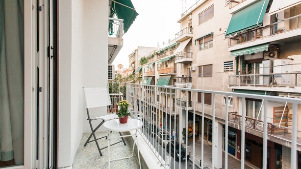 A balcony with a small table and chair, a potted plant, and a view of adjacent buildings. - Charming Acropolis Metro Apartment (Athens)