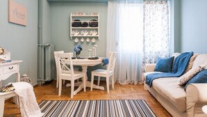A room with a dining table, chairs, a sofa, and a wall-mounted shelf with plates. - Charming Acropolis Metro Apartment (Athens)