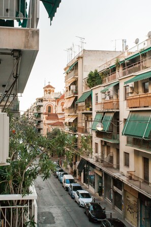 A narrow street lined with multi-story buildings, some with balconies and satellite dishes. A church with a bell tower is visible in the distance. - Charming Acropolis Metro Apartment (Athens)