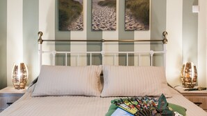 A bedroom with a white metal bed frame, two pillows, a bedside table with a lamp, and three framed pictures on the wall. - Charming Acropolis Metro Apartment (Athens)