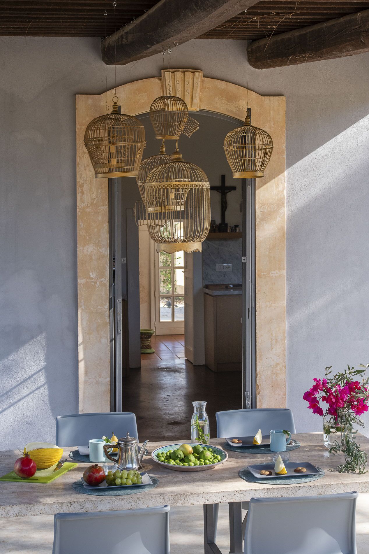 A dining area with a table set for two, a vase of flowers, and a view into the kitchen.
