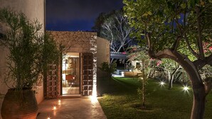 A nighttime view of a building with a brick entrance, a concrete pathway, and a tree-lined garden. - Calm and serenity in the heart of a nature reserve, 5 km from the sea. (Noto)