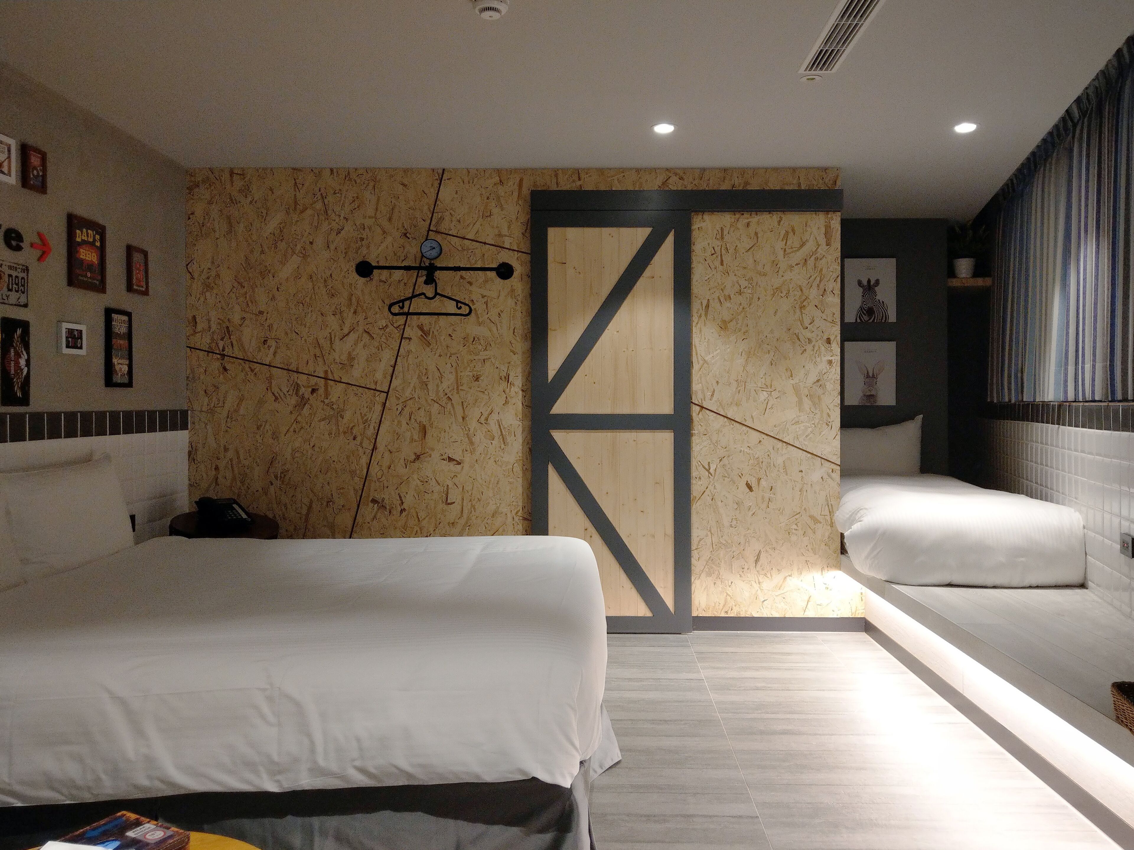 A modern hotel room with a large bed, a small bedside table, a wall-mounted clock, and a large window with curtains.