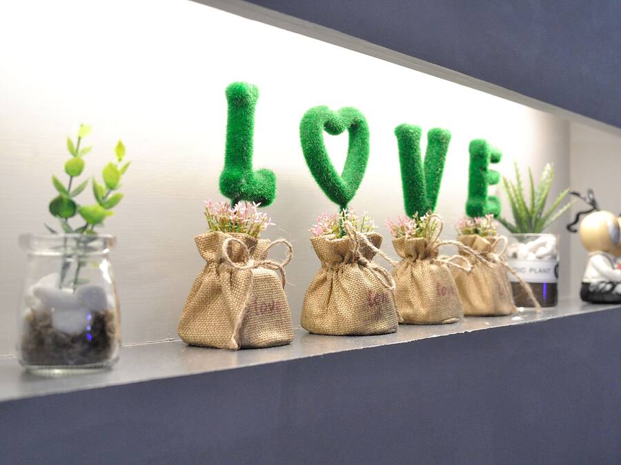 Une étagère avec des sacs en toile de jute contenant de petites plantes et une enseigne décorative qui épelle le mot « AMOUR ».