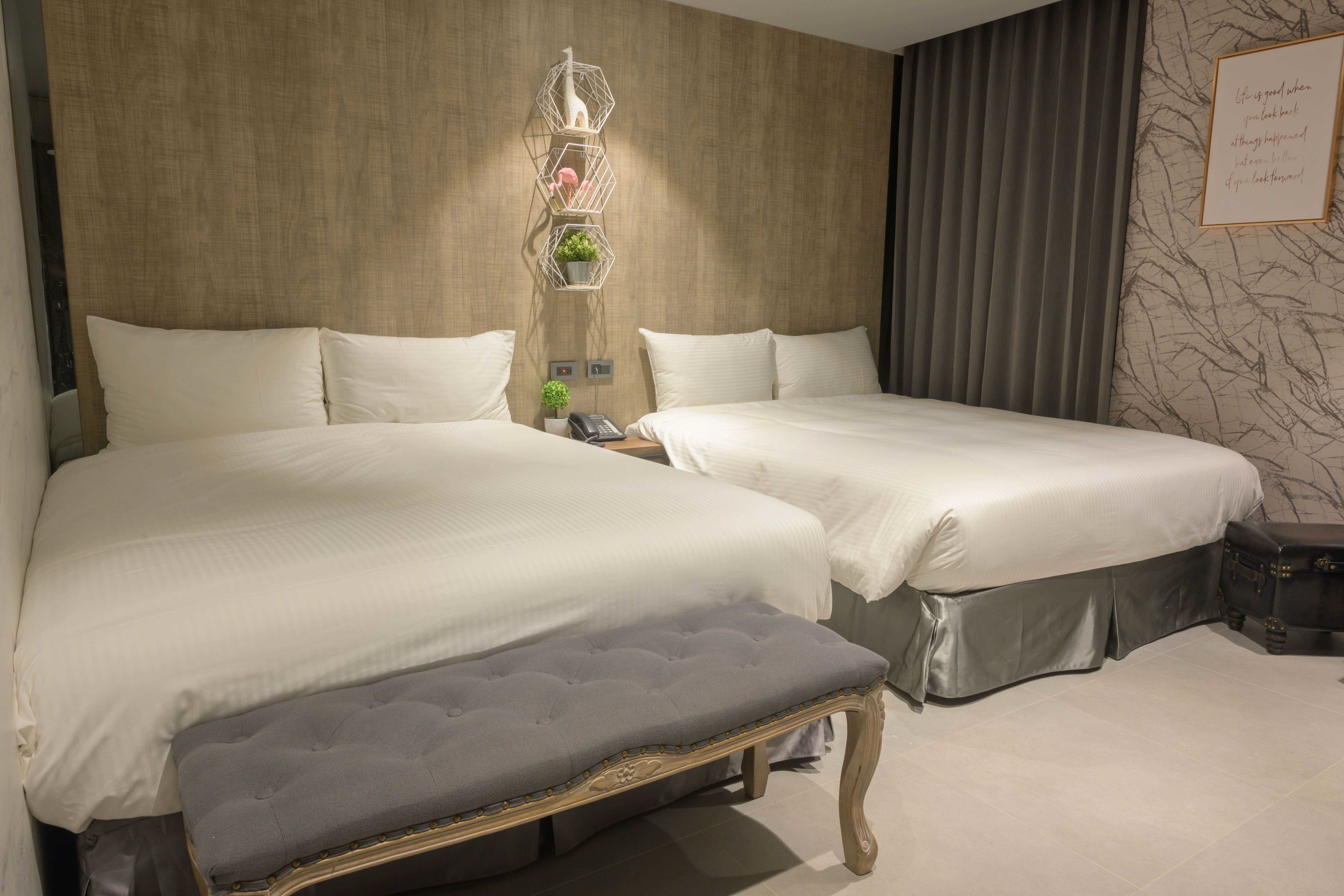 A hotel room with two beds, a bench, a telephone, and a decorative wall piece.