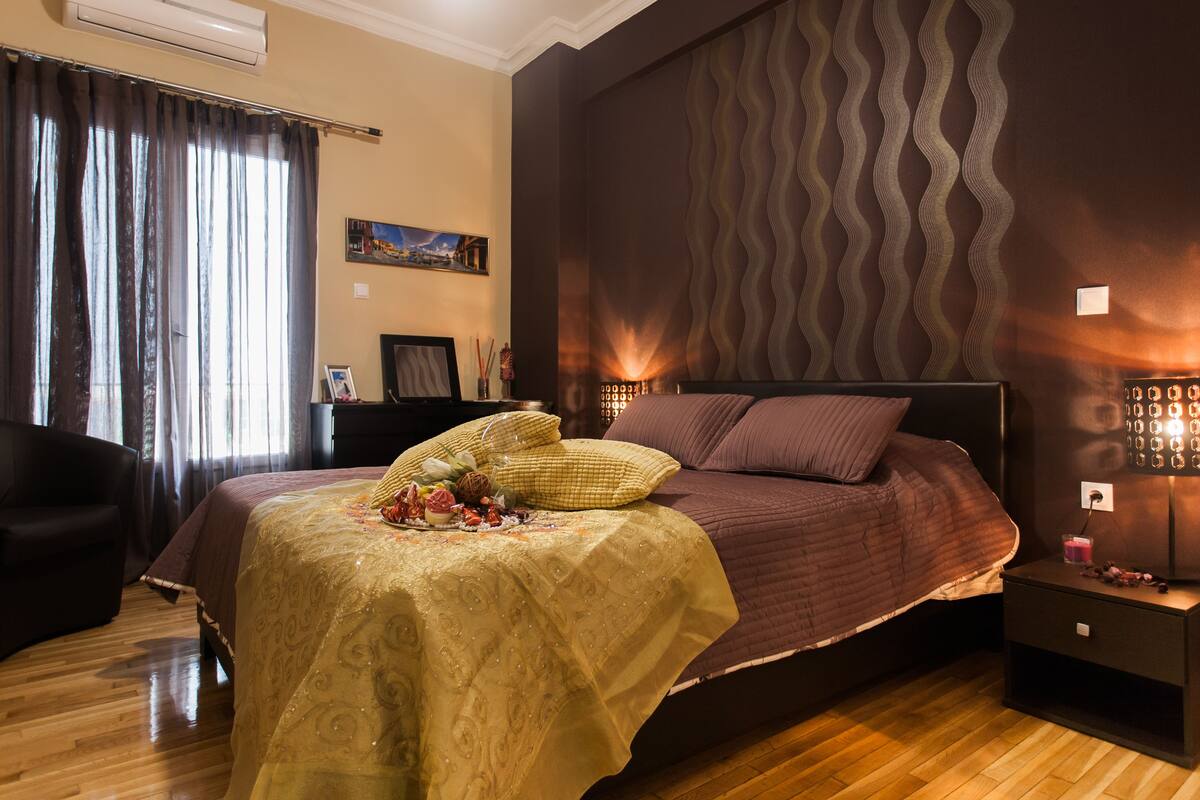 Quarto com cama, mesa de cabeceira, cadeira e parede com padrão texturizado.