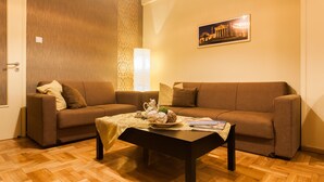 A living room with two sofas, a coffee table, and a wall-mounted lamp. - Spacious Safe Apartment Walk Acropolis (Athens)