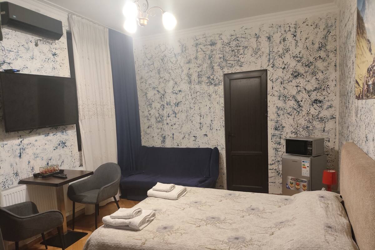 A hotel room with a bed, a desk, a chair, a TV, a microwave, and a door.