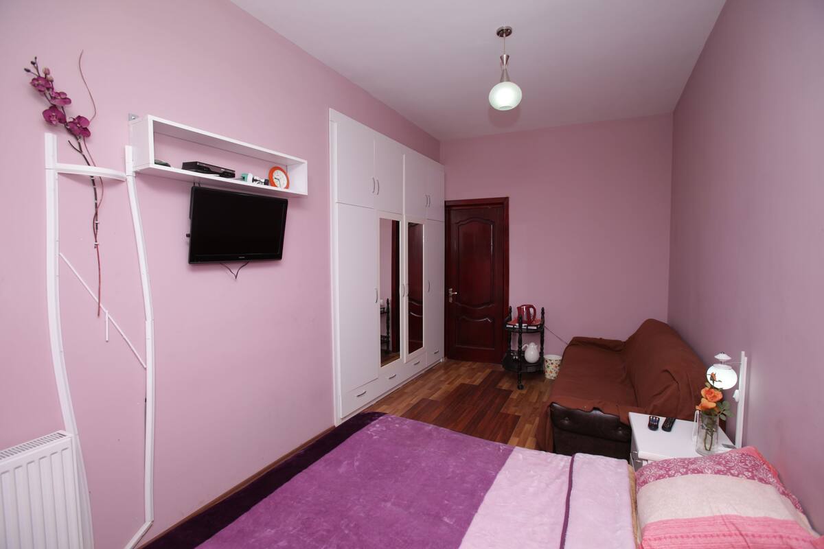 A bedroom with a bed, a wardrobe, a television, and a small table with a vase of flowers.