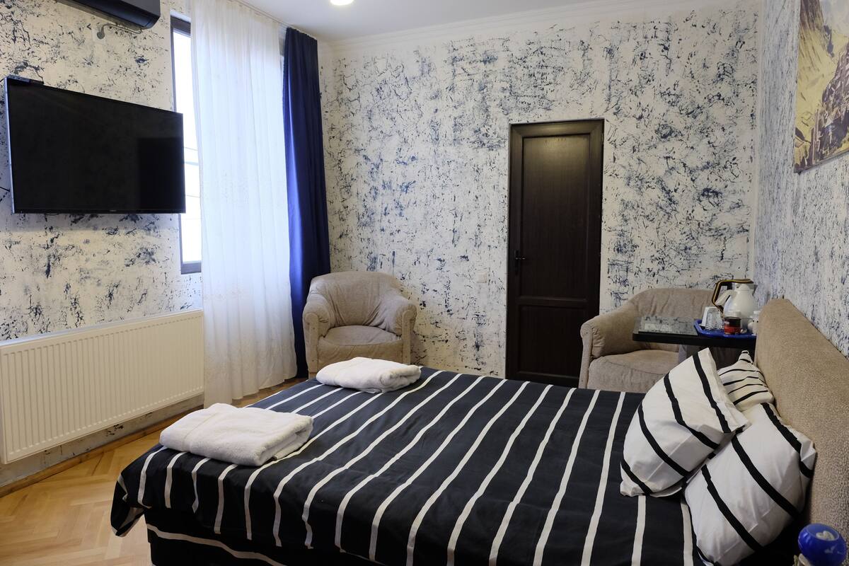 A hotel room with a bed, a chair, a desk, a TV, and a door.