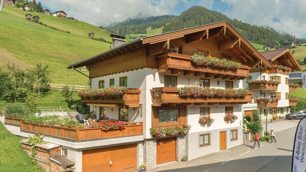 En traditionel chalet-bygning med flere balkoner dekoreret med blomsterkasser, beliggende i et bjergområde under en klar himmel.