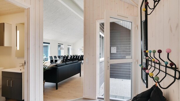 Een moderne hotelkamer met een zwarte bank, een zithoek met stoelen, een houten wand en een kapstok met gekleurde ballen.