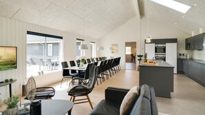 Een ruime woonkamer met een eettafel, zwarte stoelen, een bank en een keuken met moderne apparatuur.