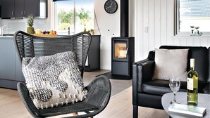 Een moderne keuken met donkere kastjes, een rieten stoel met een gestructureerd kussen, een zwarte bank met een kussen, een tafel met een fles wijn en een glas, en een klok aan de muur.