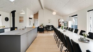 Een moderne keuken met een centraal eiland, een eethoek met een lange tafel en stoelen, en een groot raam dat natuurlijk licht binnenlaat.