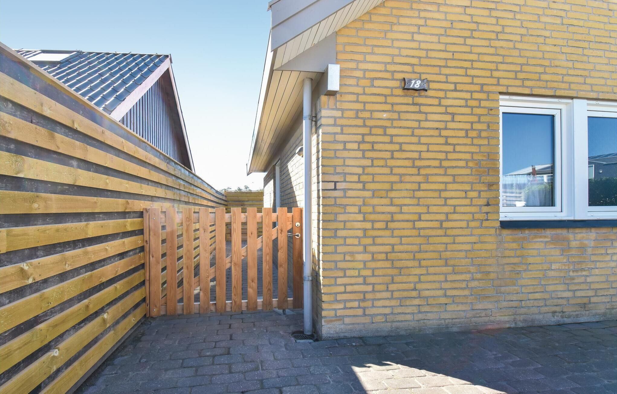 En boligbygning med facade i mursten, hegn af træ og et vindue.