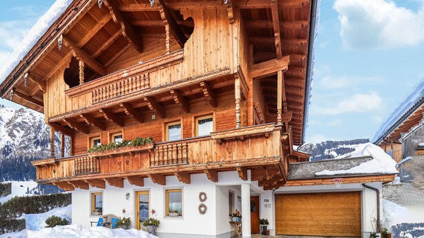 Una cabaña de madera con balcón, garaje y vistas a montañas nevadas.