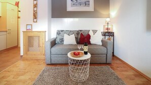 Una sala de estar acogedora con un sofá gris, una mesita redonda pequeña y un cuadro enmarcado sobre el sofá.