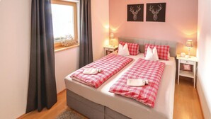 Una cama doble con ropa de cama a cuadros rojos y blancos, dos mesitas de noche con lámparas y una ventana con cortinas.