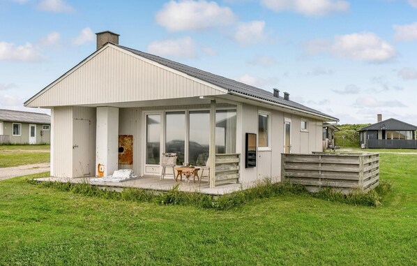 Situated on a grassy area, this single-story building features a covered porch with a table and chairs for outdoor dining or relaxation.