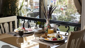 A breakfast table with a variety of dishes, a vase with dried plants, and a view of the street outside. - Sapphire Inn (Baku)