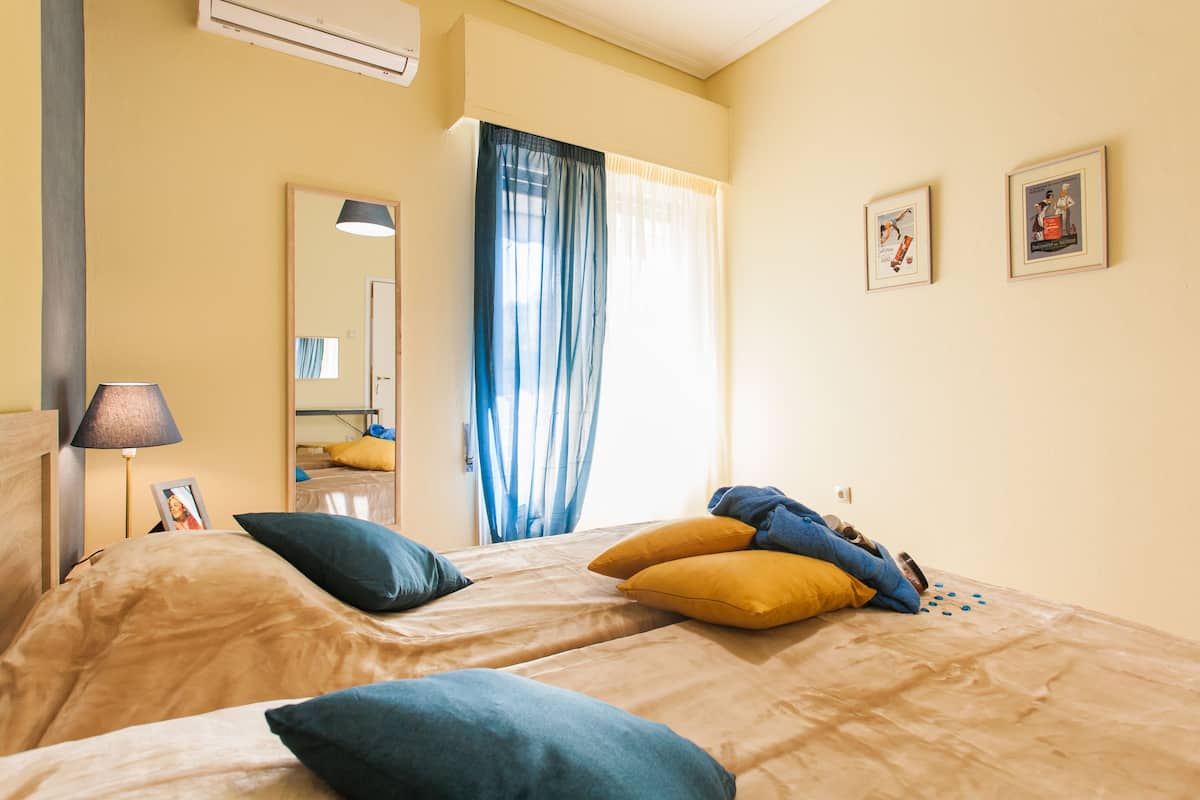 A hotel room with two beds, a mirror, a lamp, and a window with curtains.