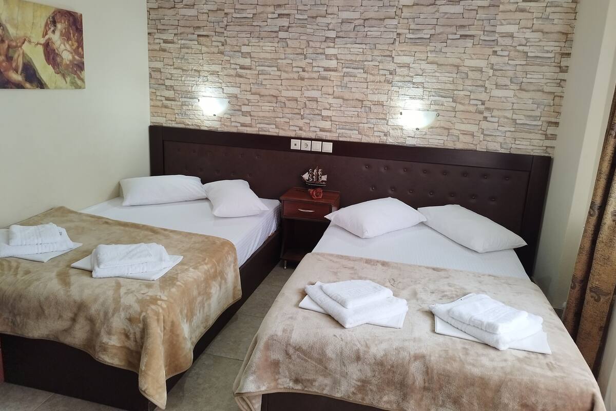 A hotel room with two beds, each with white linens and a brown blanket. There is a wooden headboard with a light fixture above.