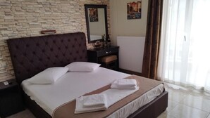 Una cama bien hecha con cabecera marrón, una mesita de noche con espejo y una ventana con cortinas.