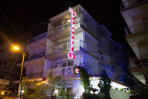 A multi-story hotel with balconies, a neon sign, and a street lamp. - Hotel Villa Pigasos (Katerini)