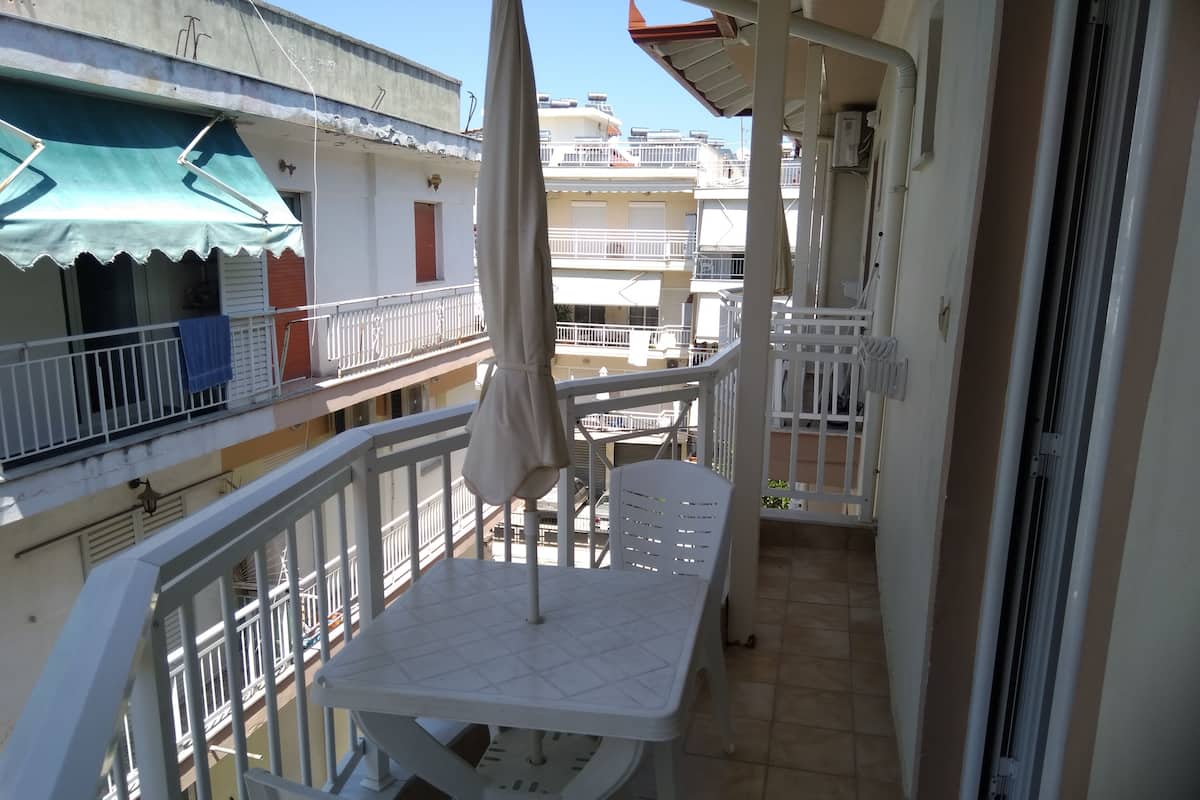 A balcony with a white table and chairs, a white umbrella, and a view of neighboring buildings.