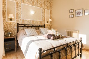 Um quarto com cama, mesas de cabeceira, luminárias fixadas na parede e quadros emoldurados.