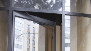 A modern building entrance with a glass door, a visible staircase, and a reflection of a street scene including parked cars and a building with a sign that reads "AVIS". - Central Apartment near Acropolis (Athens)