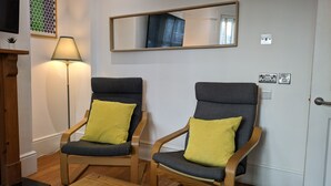 To træstole med gråt betræk og gule puder, placeret foran en hvid dør med et spejl over.