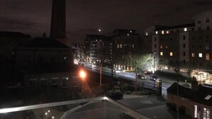 A nighttime cityscape with a prominent clock tower, illuminated buildings, and a busy street.