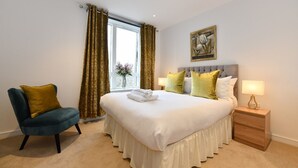 A neatly arranged bedroom with a bed, a chair, a nightstand, and a window with curtains.