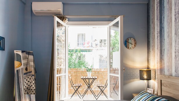 A bedroom with a bed, a bedside table, a lamp, a view of the outside, and a window. - Central Quiet Safe Apartment (Athens)