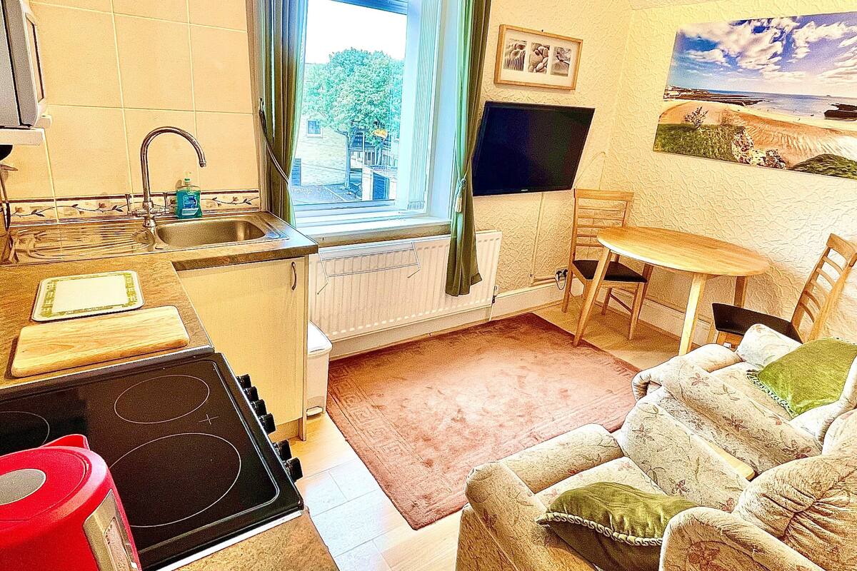 A compact kitchen with a window, a dining area with a table and chairs, and a sofa.