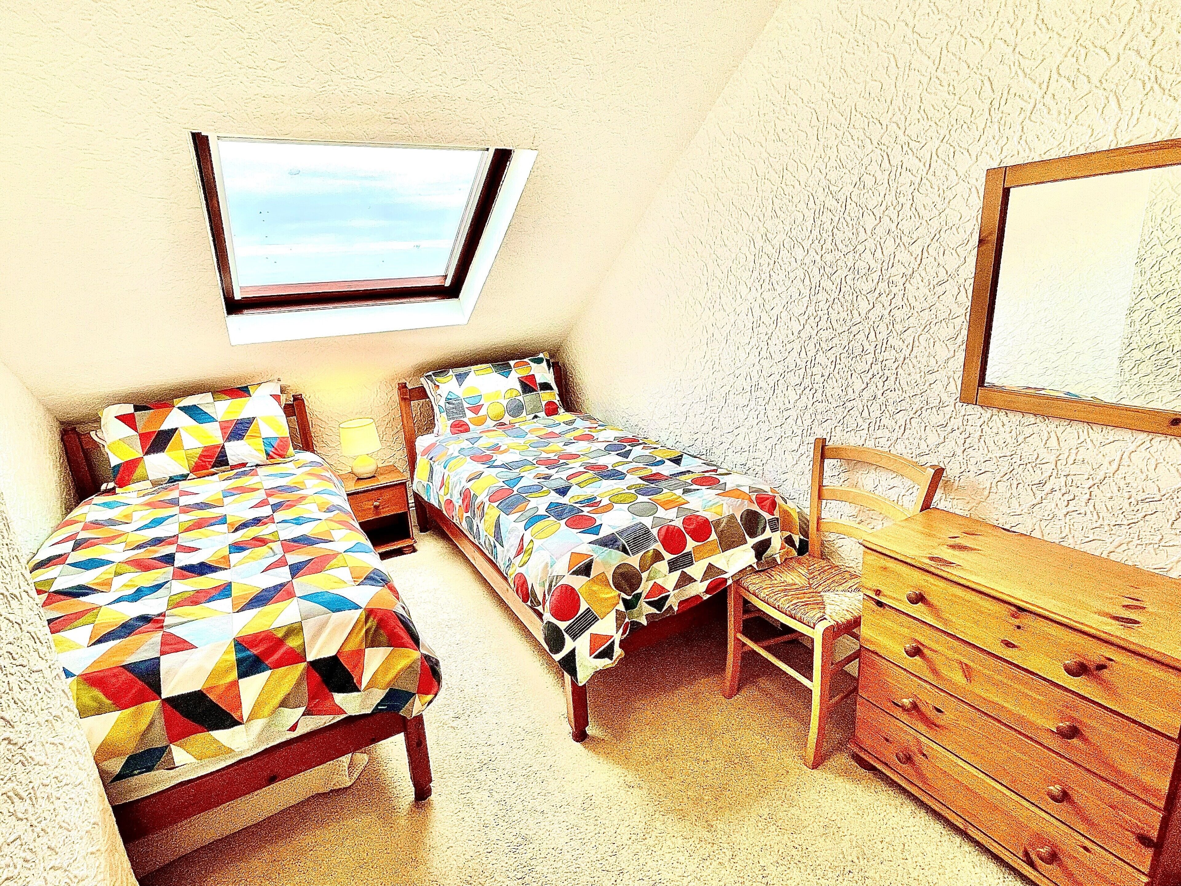 A small, cozy bedroom with two beds, a dresser, and a skylight.