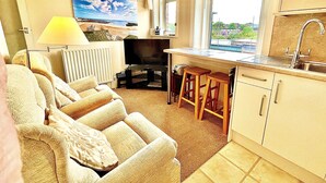A compact living space with a sofa, a TV, a small kitchen area, and a window with a view. - Seafront Apartments (North Shields)