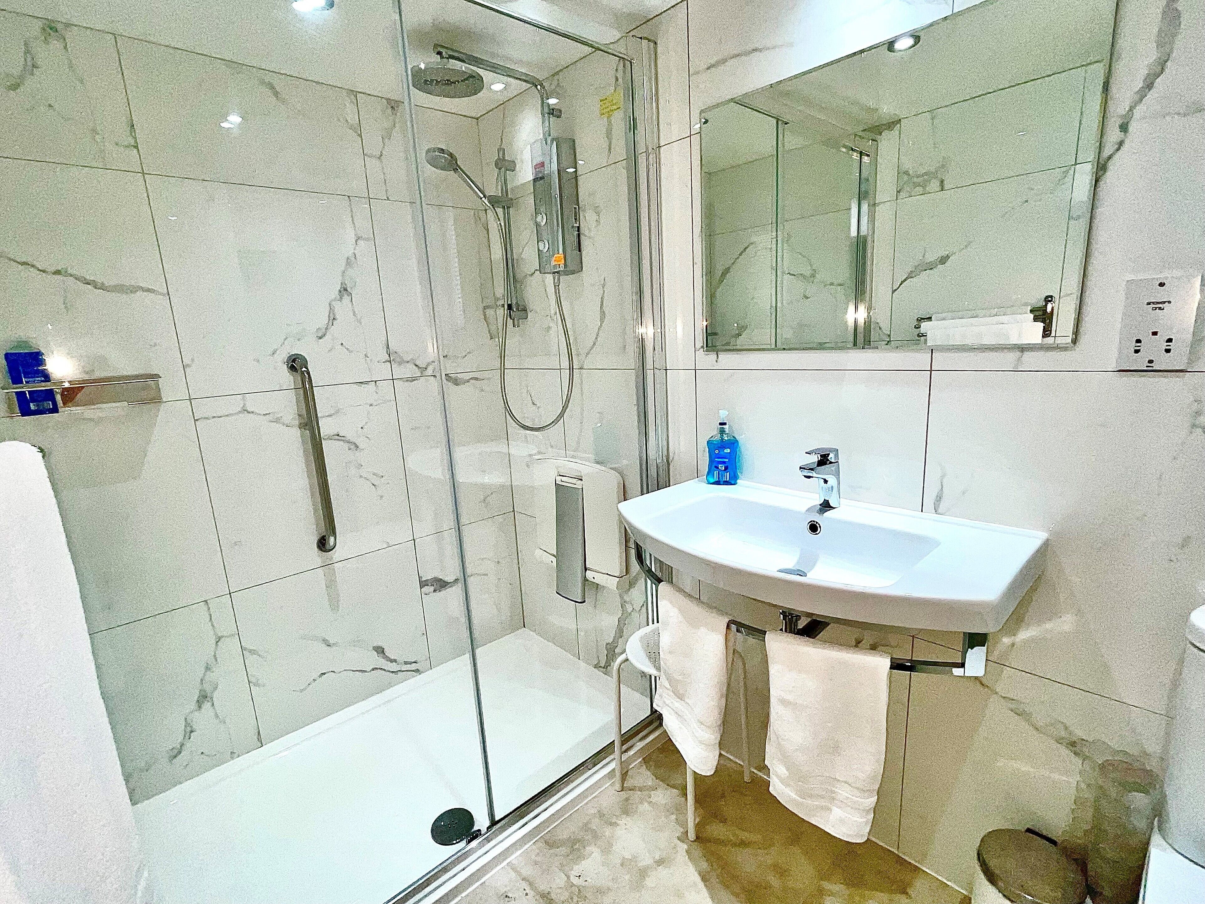 A modern bathroom with a glass-enclosed shower, a white sink, and a large mirror.
