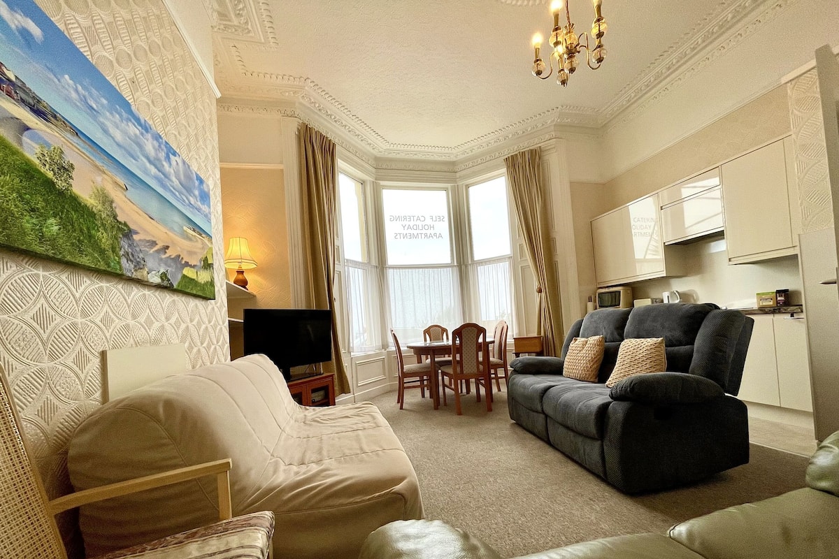 A living room with a sofa, a television, and a dining area with chairs and a table.
