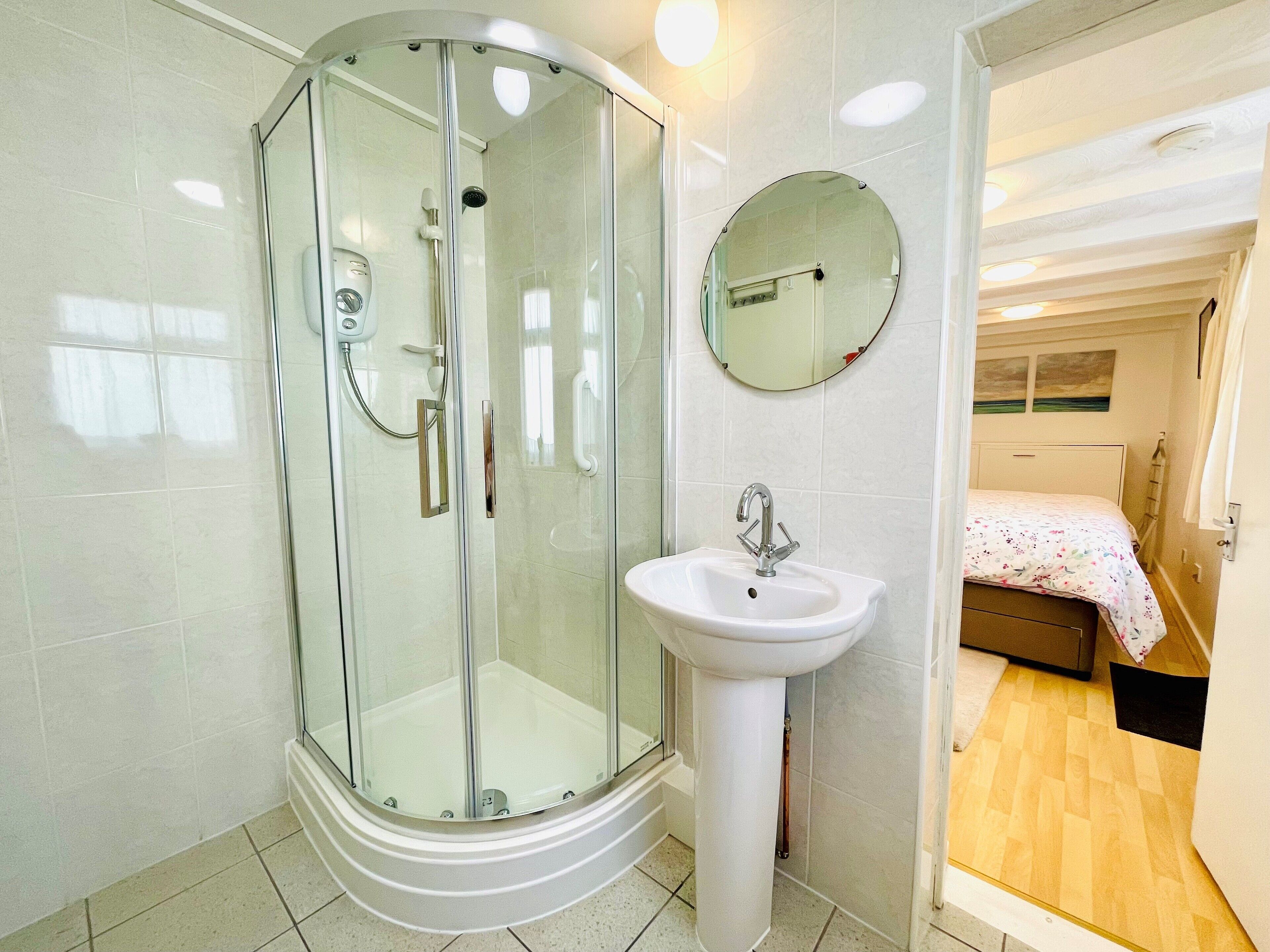 Une salle de bain moderne avec une douche à parois de verre, un lavabo sur colonne et un miroir rond.